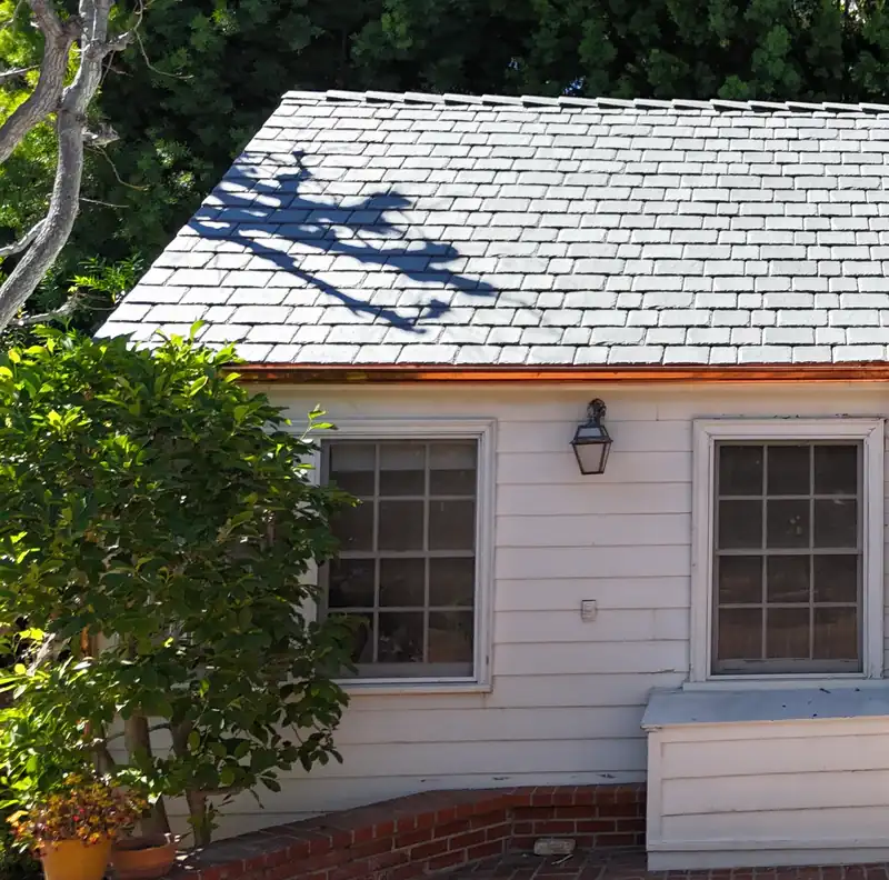 White clapboard cottage wing with a new copper gutter along its eave
