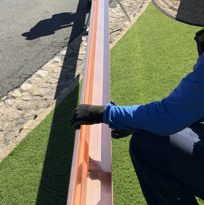 One of our installers steadying a long run of new copper gutter on stands at the curb