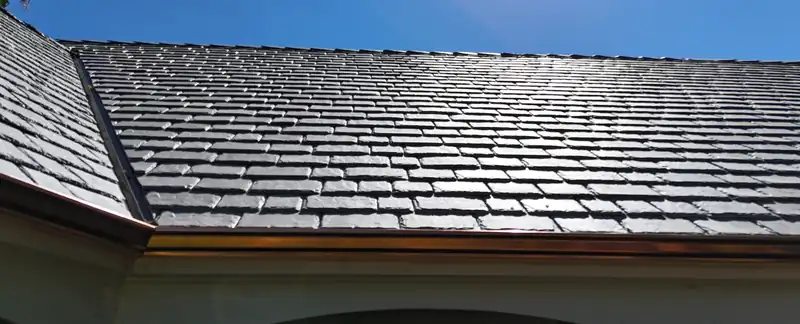 Two copper gutter runs meeting at a corner below a gray slate-look roof