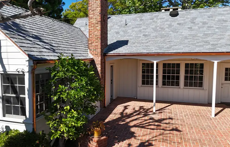 Copper gutters on several eaves around a brick patio, with a tall brick chimney between the roofs