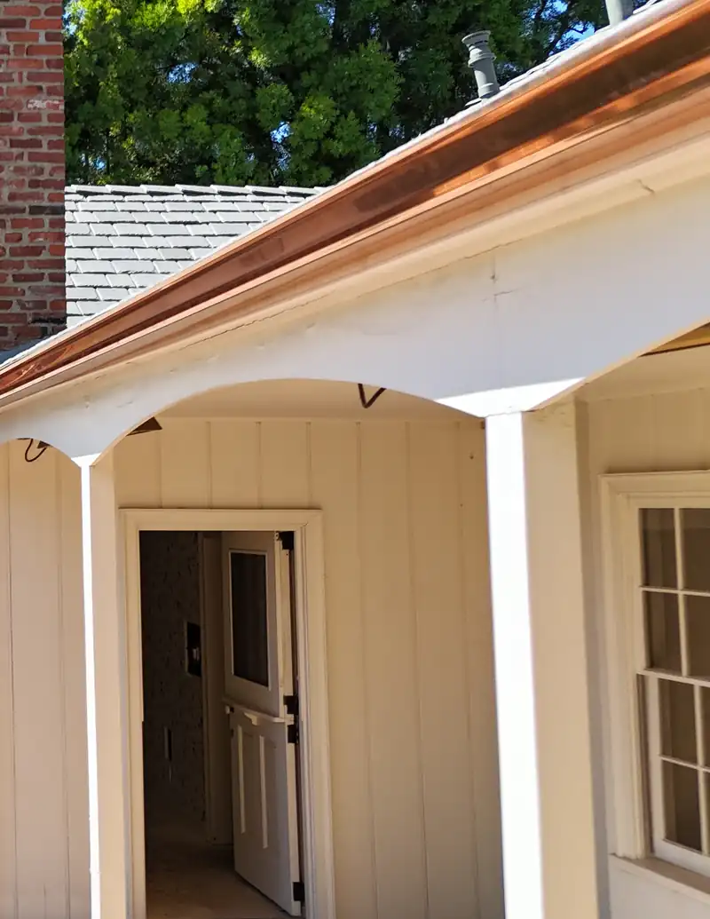 Copper gutter wrapping the eave of a covered porch on a cream board-and-batten house