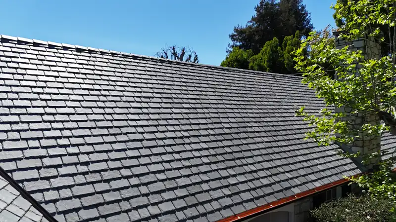 Copper gutter finishing the eave of a gray slate-look roof under tall trees