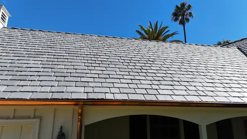 New copper gutter and downspout along the eave of a slate-look roof, palms against a blue sky